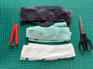3 Stoffstreifen, eine Klammer und eine Schere